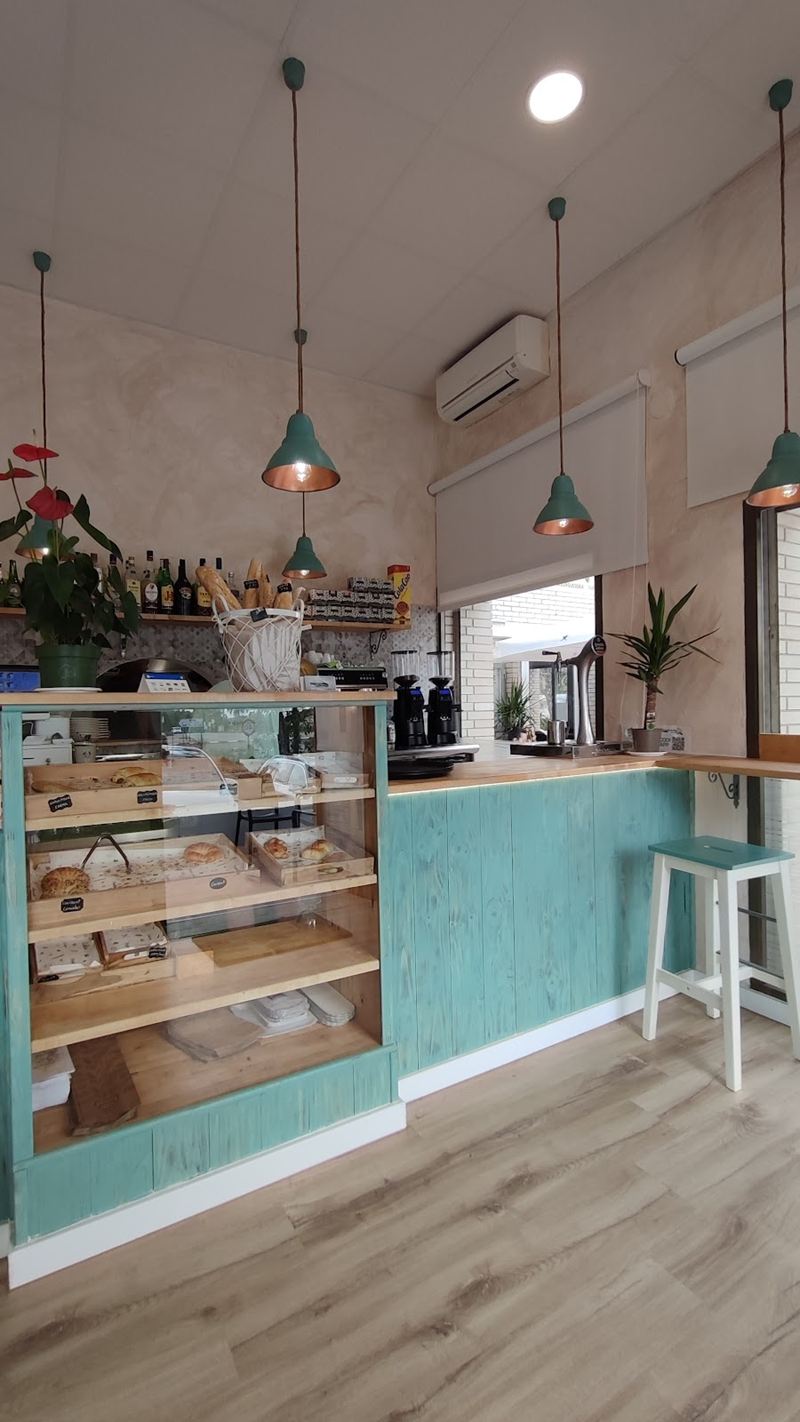 Interior de K Dolç: barra de madera turquesa, lámparas colgantes y vitrina de pastas